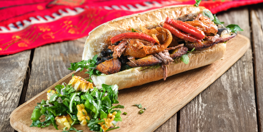 a sandwich with meat and vegetables on a wooden board