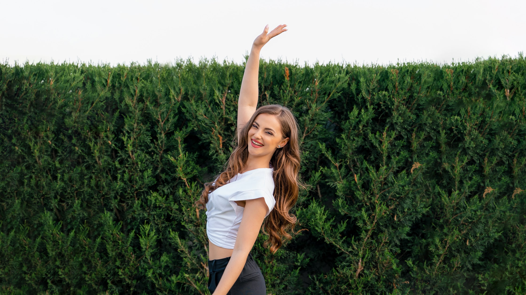 a woman with her arm raised in front of a hedge