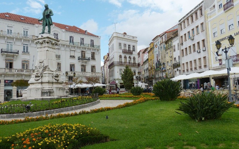 a green lawn with flowers and a statue in the middle of a city