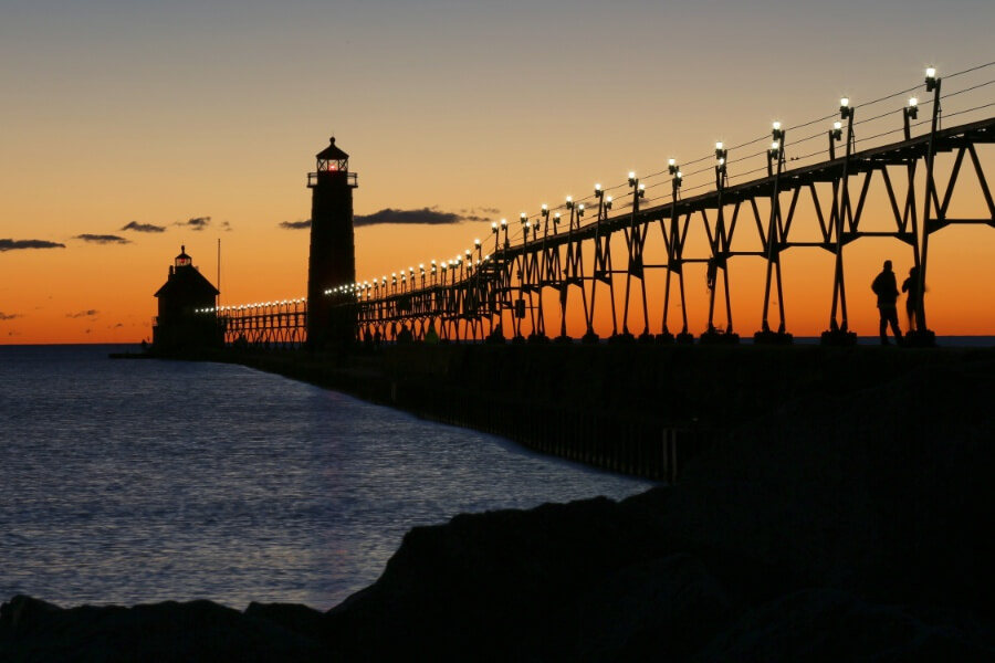 a long bridge with lights on it and a lighthouse in the background