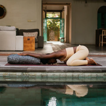 a woman doing yoga on a mat near a pool