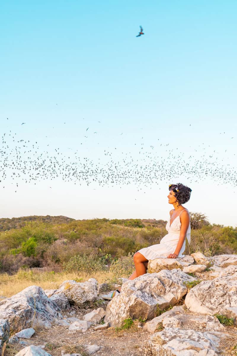 a woman sitting on rocks with birds flying in the air