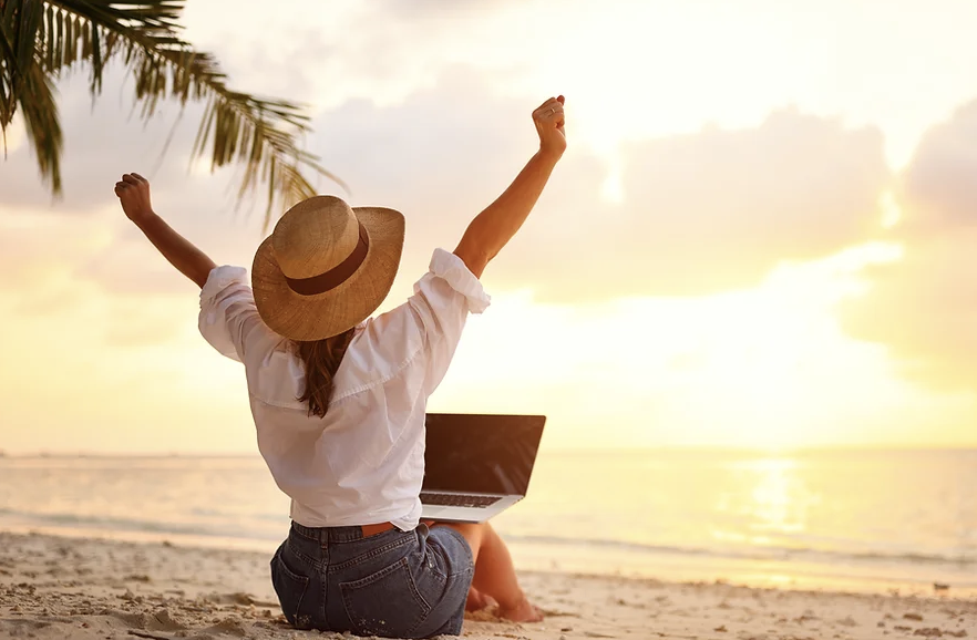 a woman sitting on the beach with her laptop
