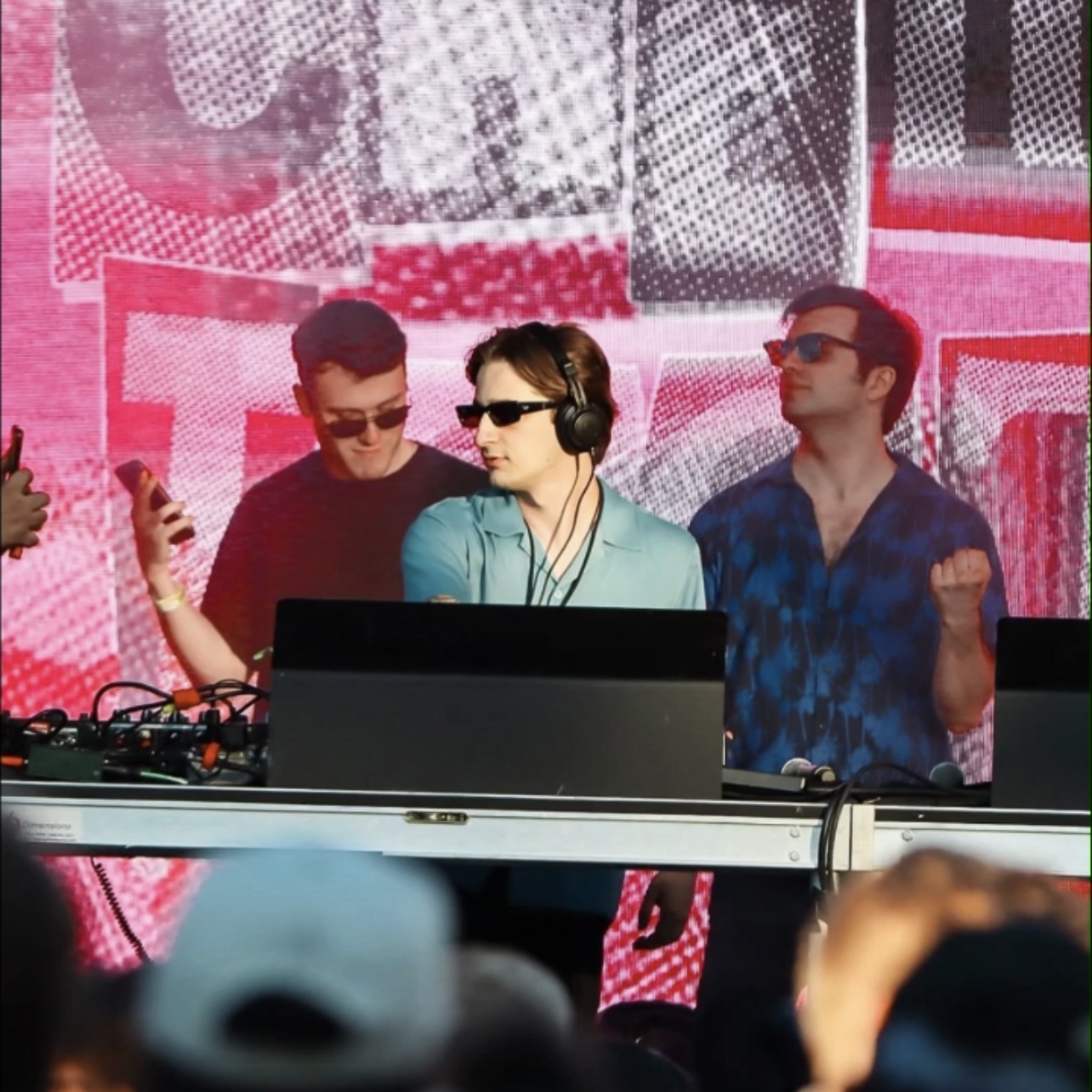 a man wearing headphones and a microphone and a man standing behind a desk with a group of people behind him