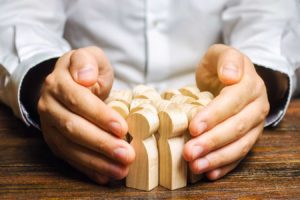 a person's hands protecting a group of wooden figures