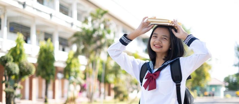 a girl in a school uniform holding books on her head