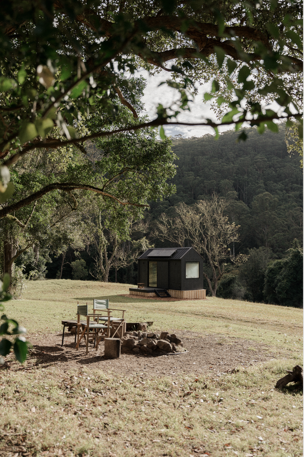 a small black building in a grassy area with a fire pit and chairs