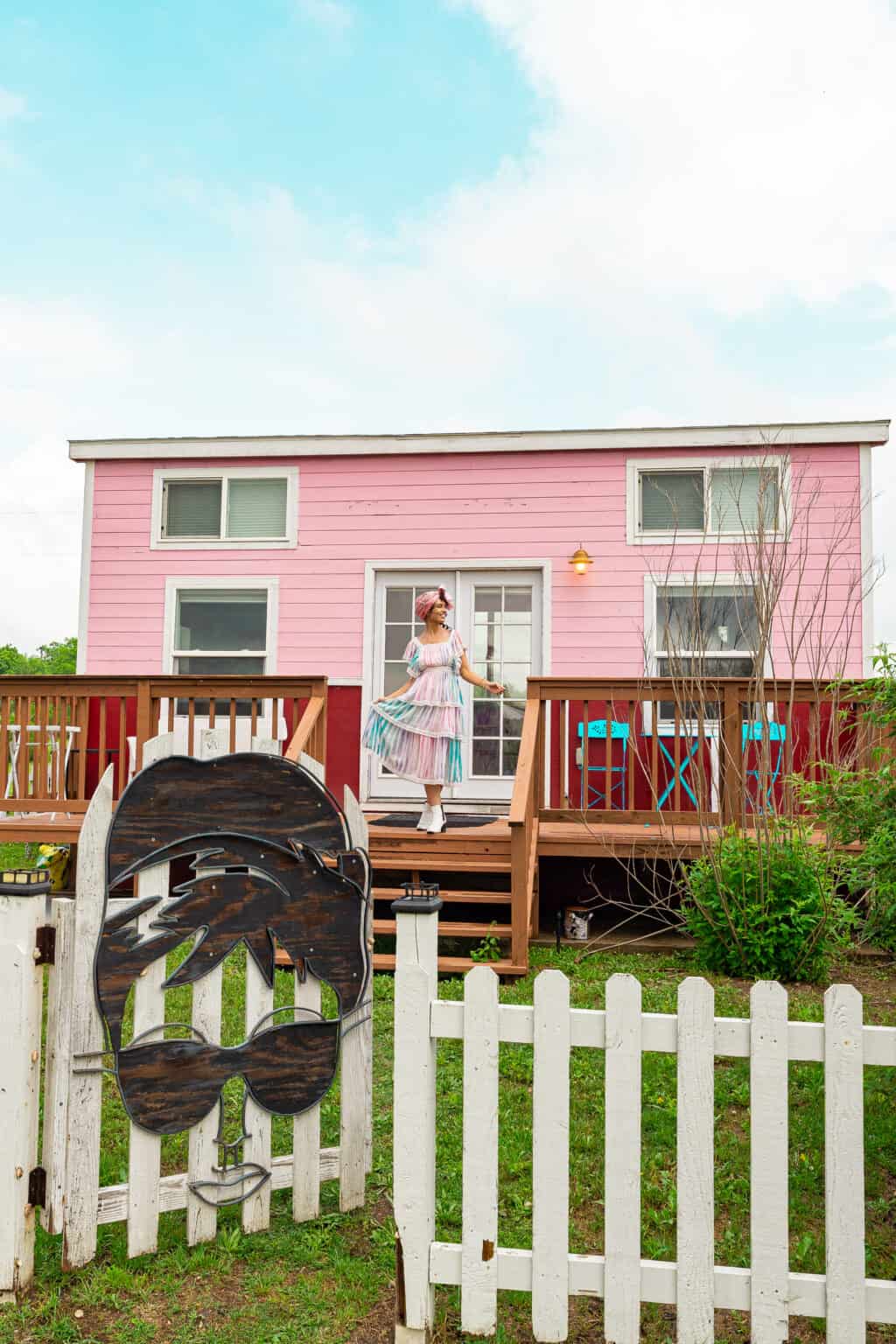 a woman in a dress standing on a deck in front of a pink house