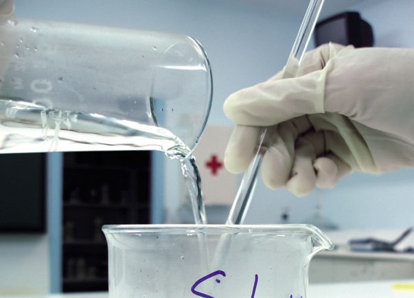 a hand pouring liquid into a beaker