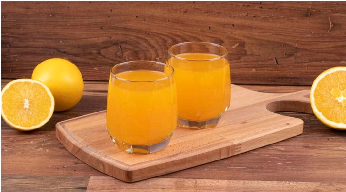 two glasses of orange juice on a wooden board