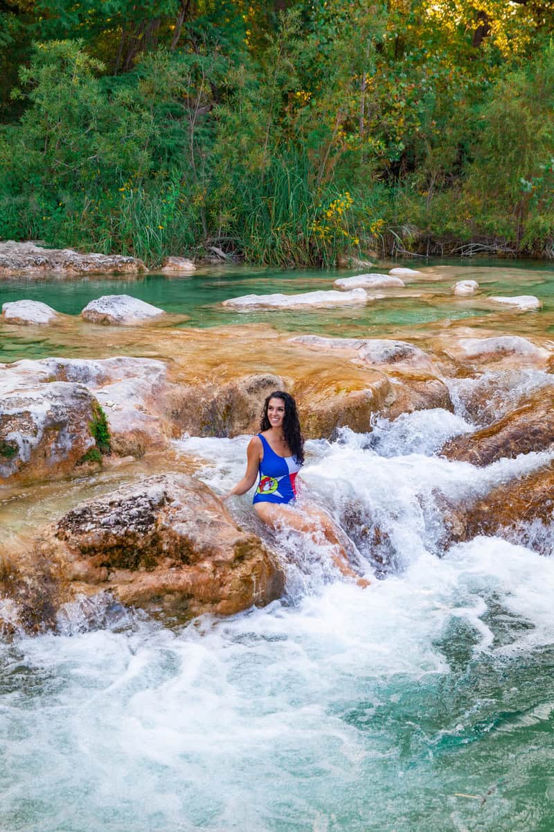 a woman in a swimsuit sitting on rocks in a river