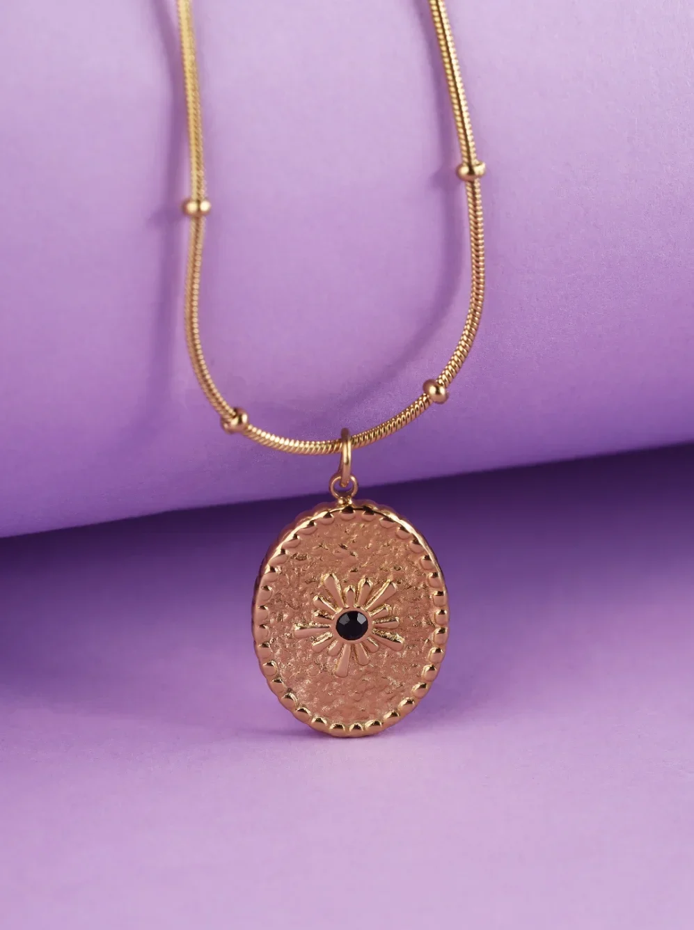 a gold necklace with a sun pendant on a purple background