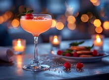 a glass of pink liquid with a plate of food and candles