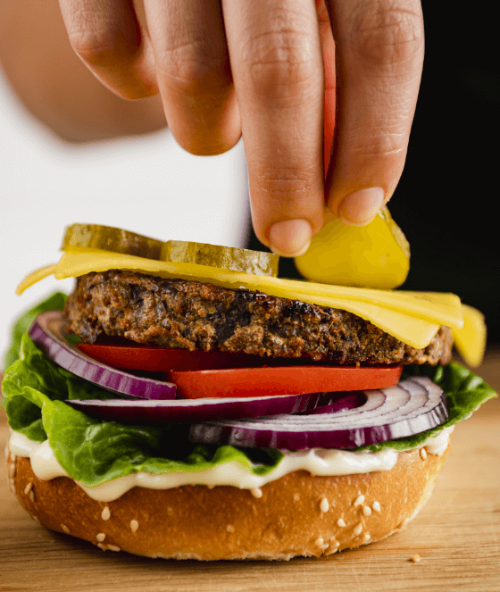 a person putting a pickle on a burger