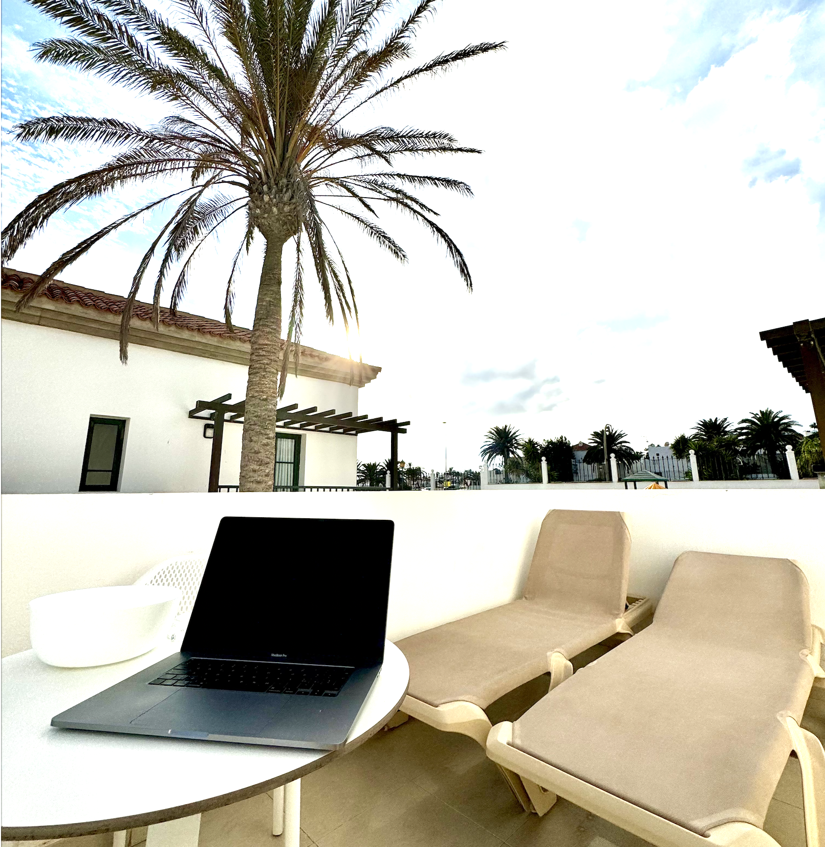 a laptop on a table with chairs and a palm tree