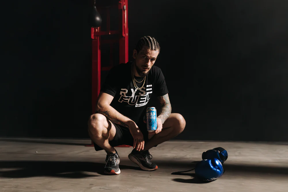 a man squatting with a can of beer and boxing gloves