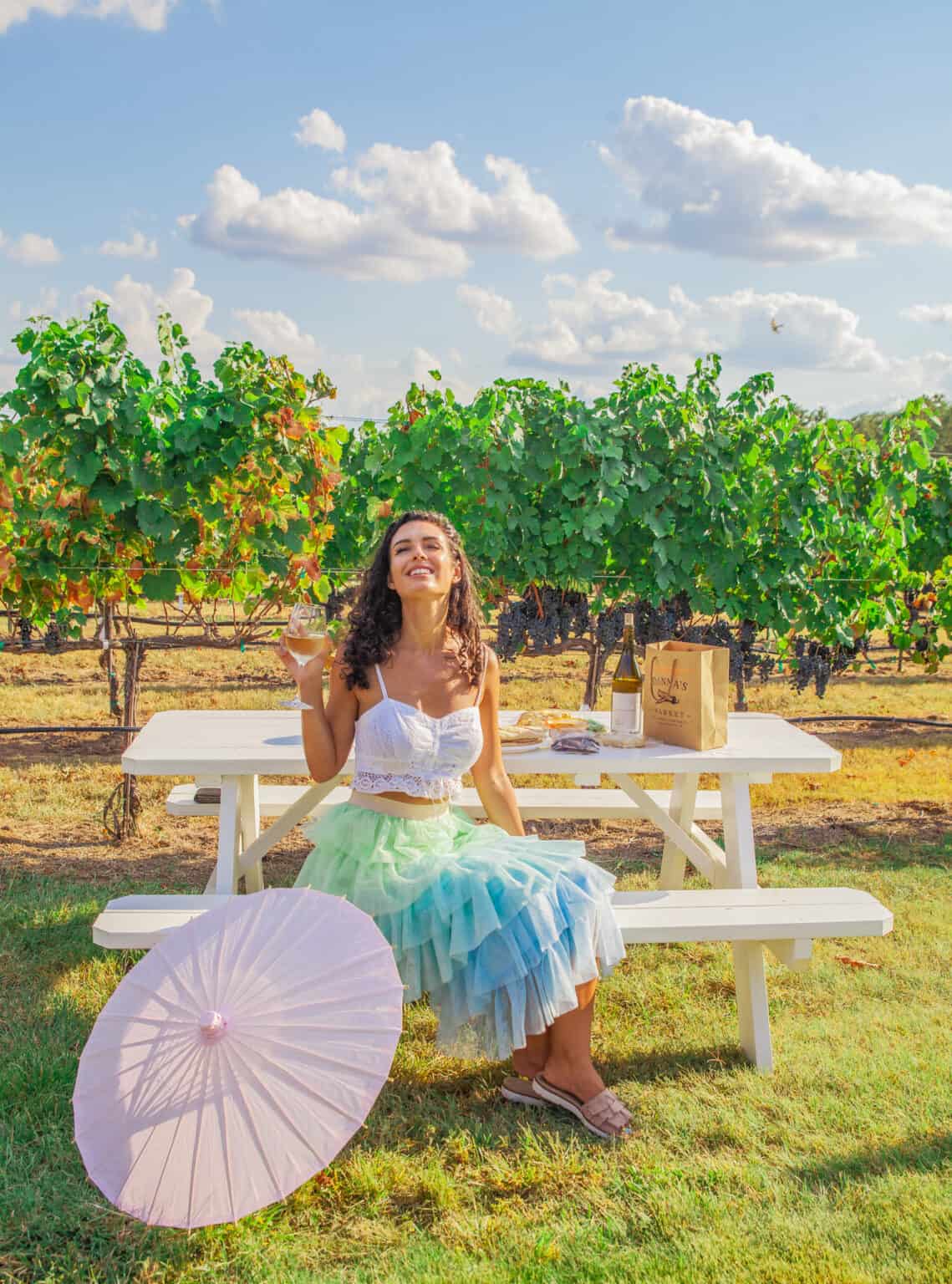 a woman sitting at a picnic table with a umbrella and a glass of wine