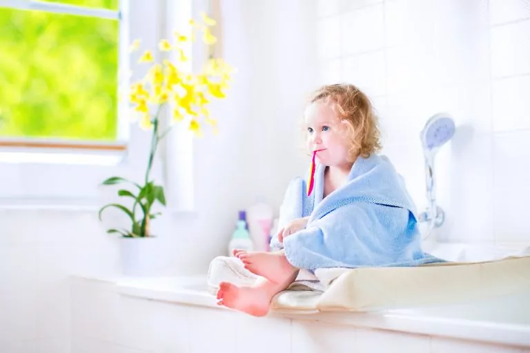a child in a bath towel brushing her teeth