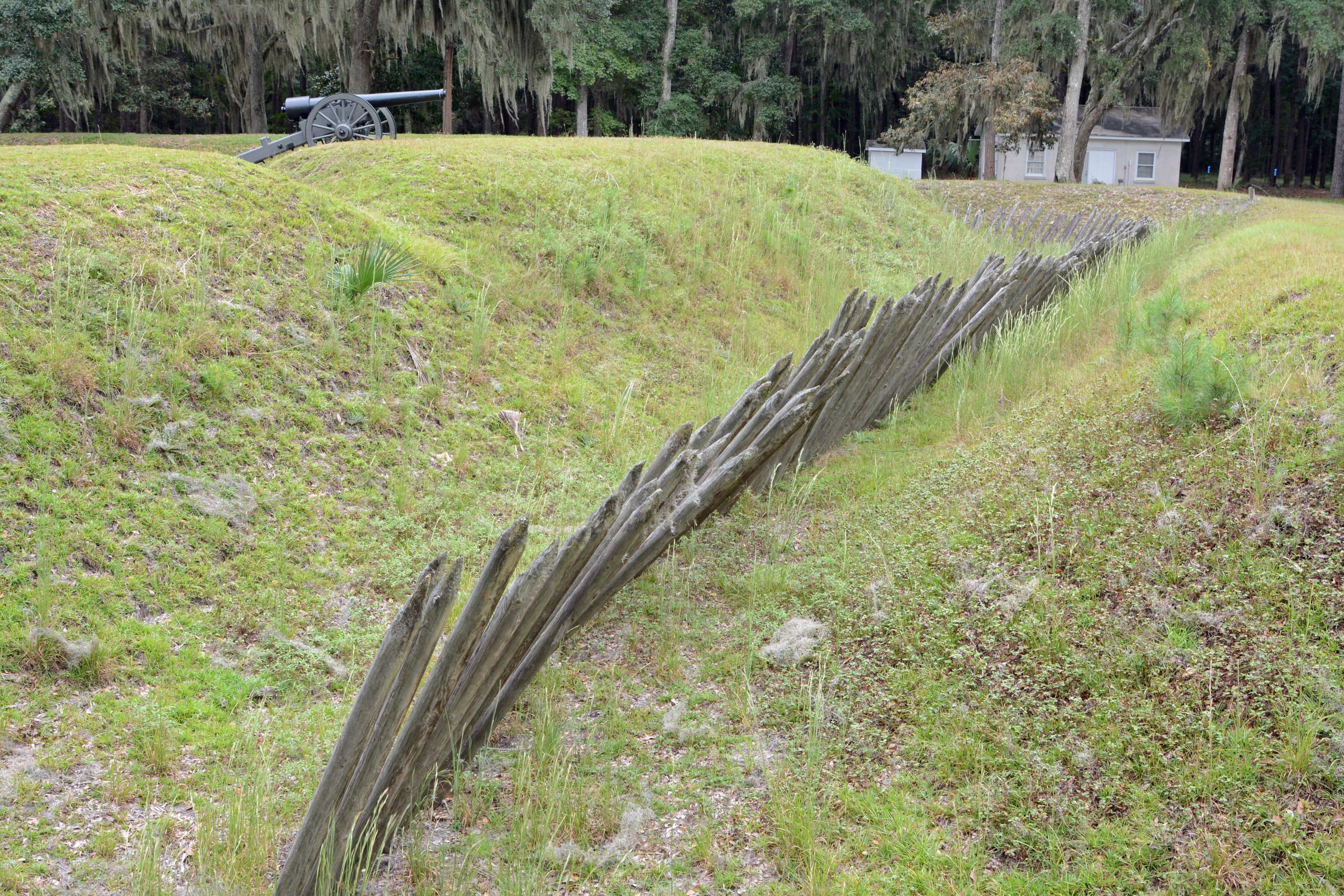a long wooden fence on a hill with a cannon in the background