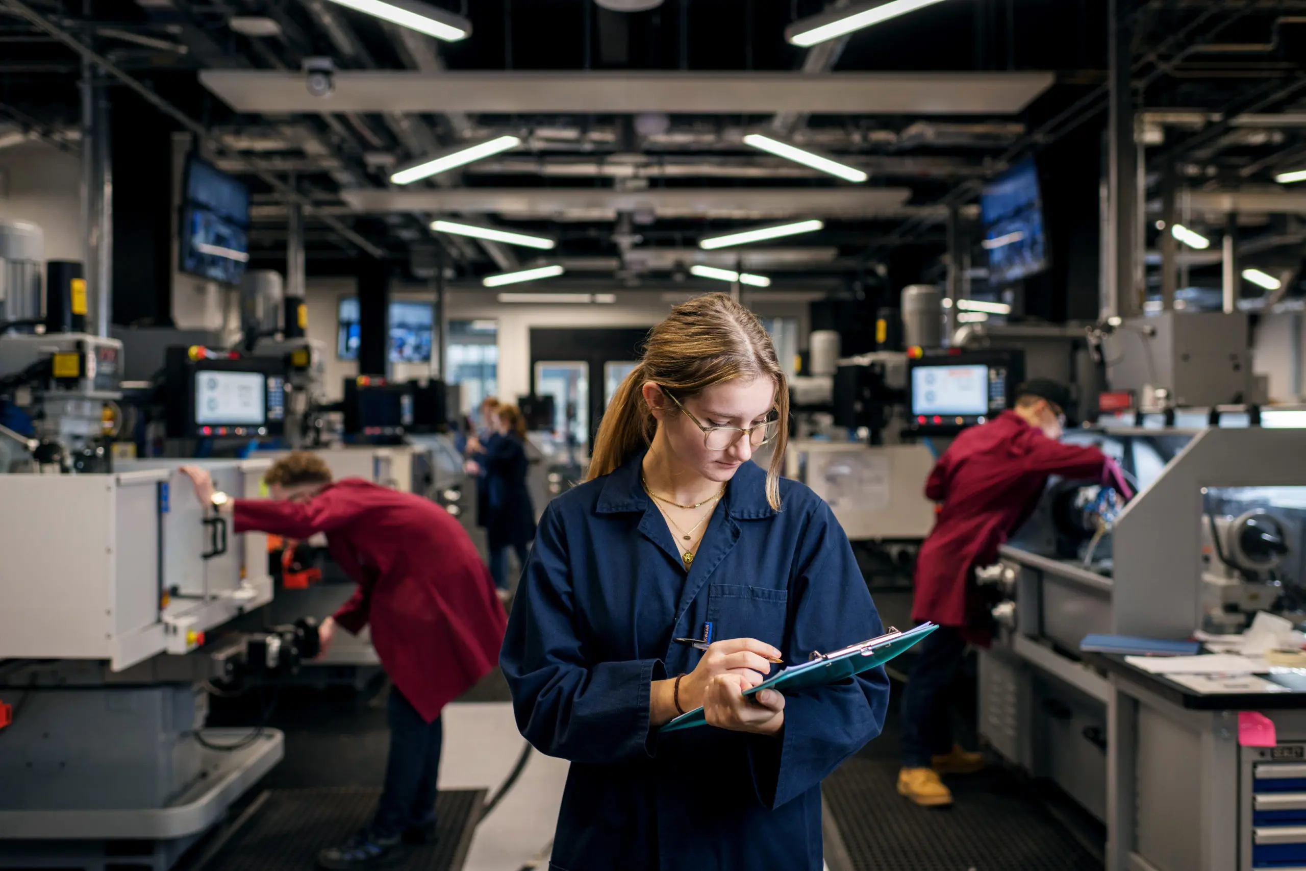 a woman in a blue coat writing on a clipboard in a factory