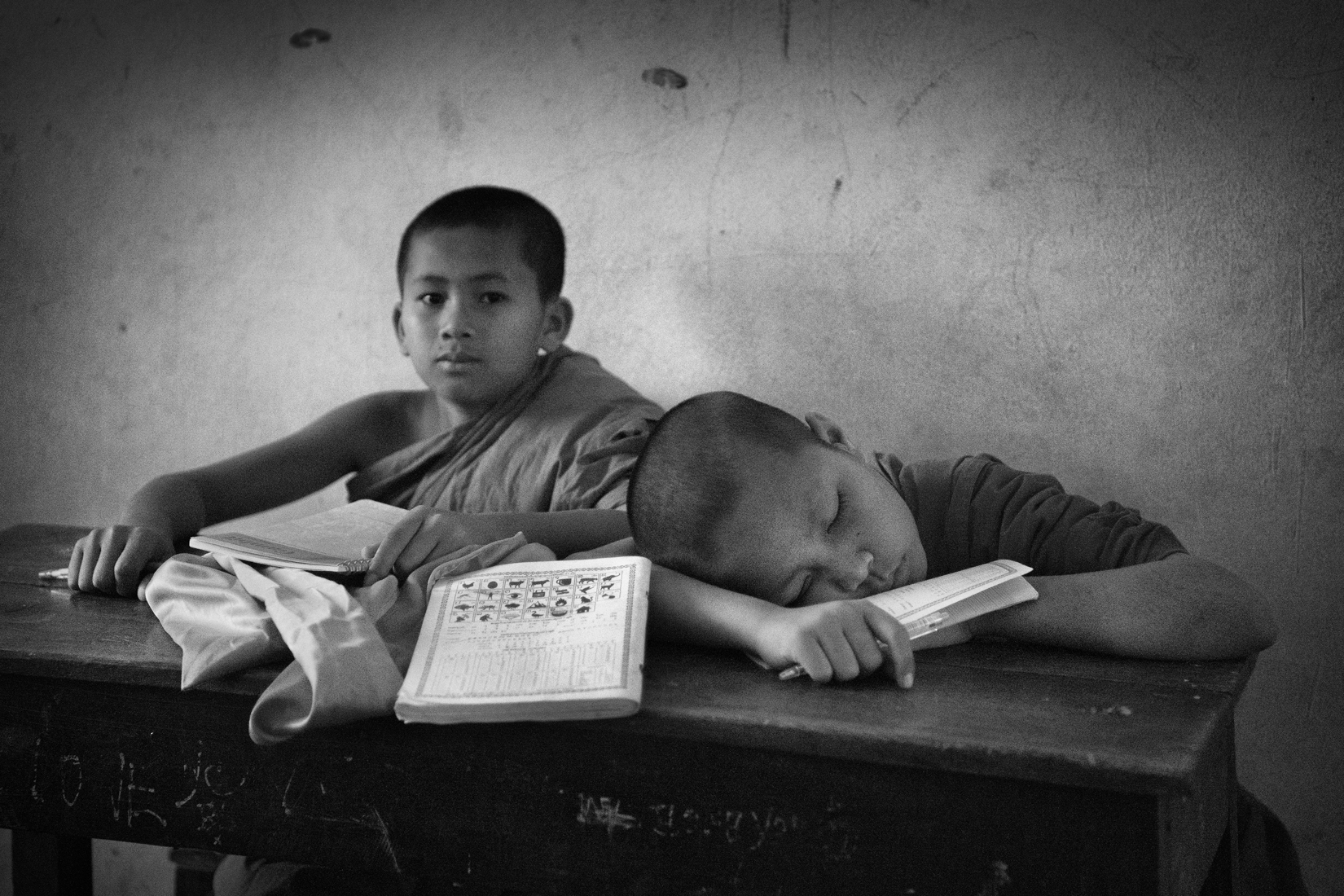 a boy sleeping on a desk next to another boy