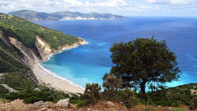 a beach with trees and blue water with Myrtos Beach in the background
