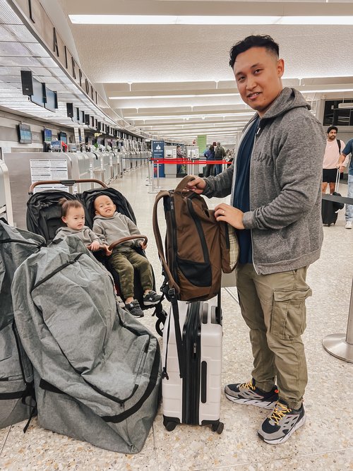 a man holding a backpack with two babies in a stroller