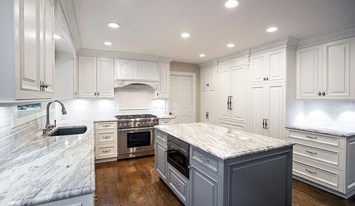 a kitchen with white cabinets and marble island
