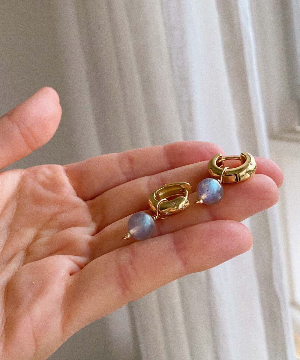 a hand holding a pair of gold earrings