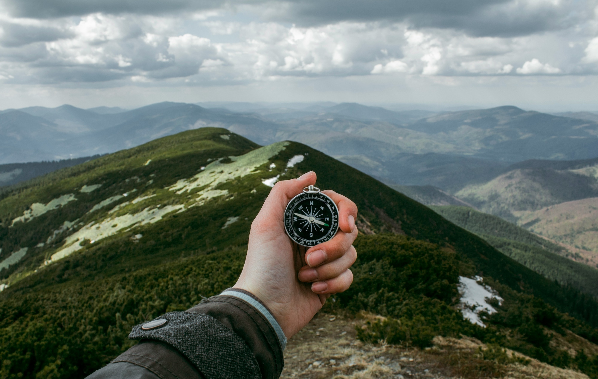 a hand holding a compass on a mountain