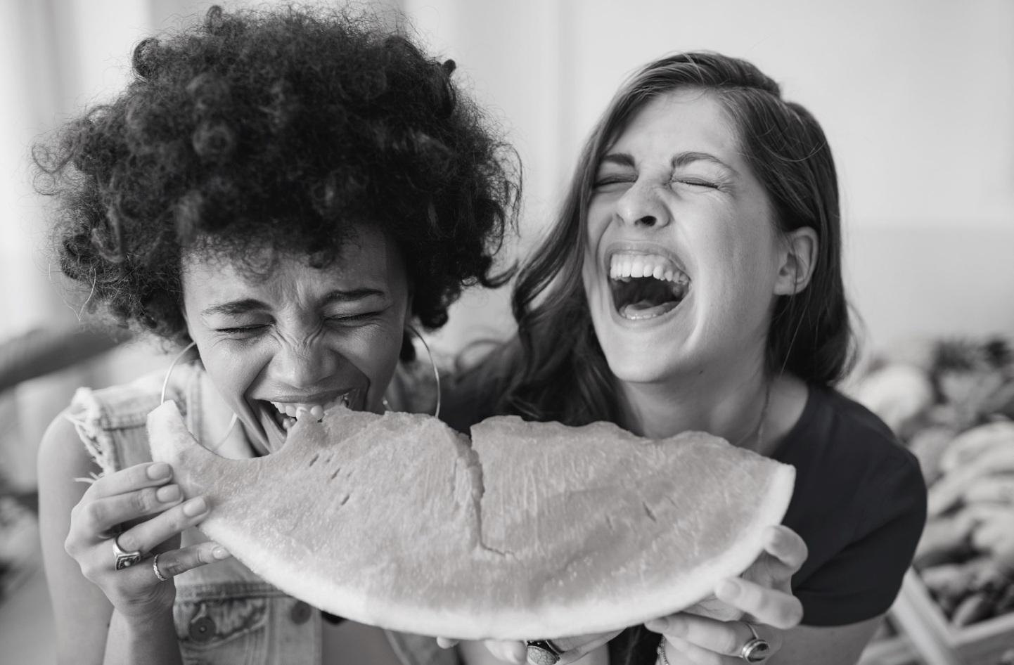 two women laughing and holding a slice of watermelon