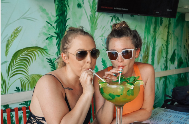 two women drinking from a large glass with straws