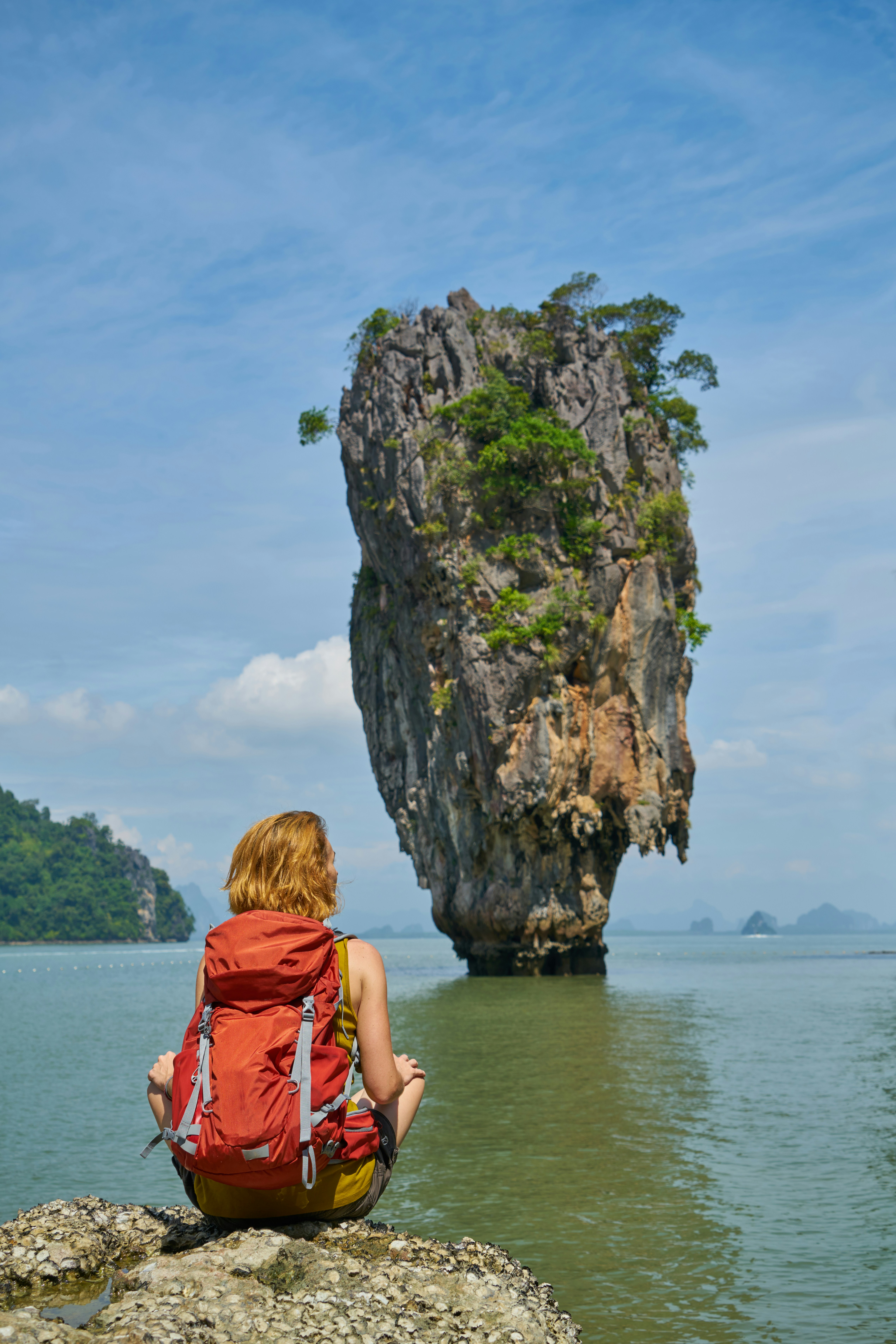 a woman sitting in the water looking at a tall rock formation