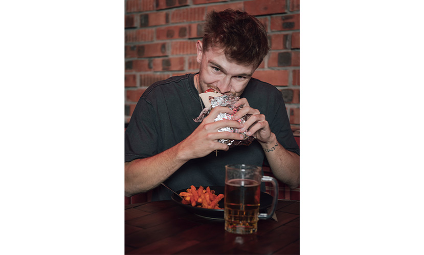 a man eating a sandwich and drinking beer