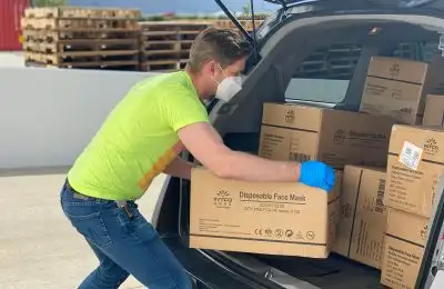 a man wearing a mask and gloves loading boxes into a van