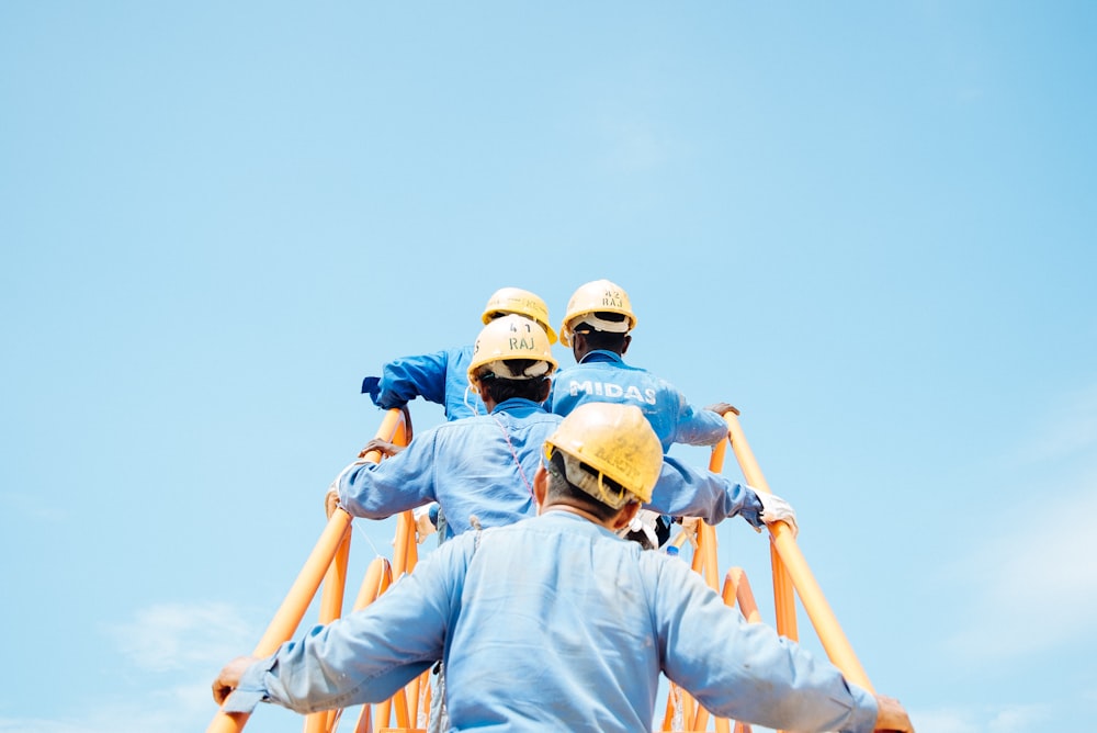a group of men wearing hard hats climbing up a ladder