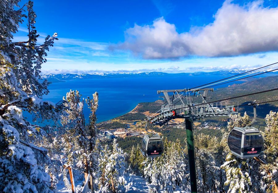 a cable car going up a mountain with snow and trees and a body of water
