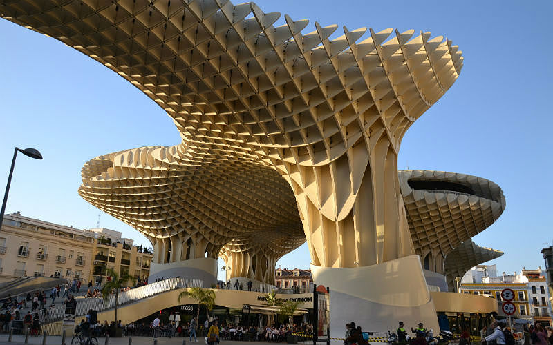 a large structure with many people walking around with Metropol Parasol in the background
