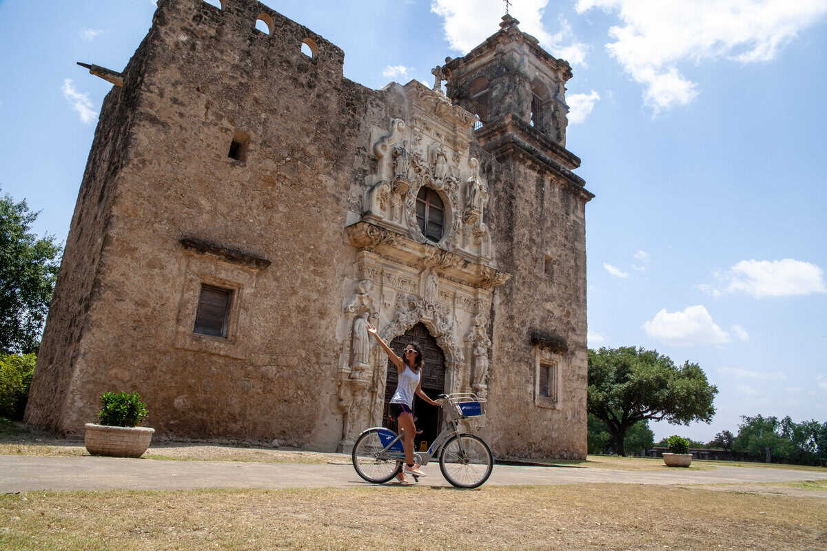 a woman riding a bicycle in front of a stone building