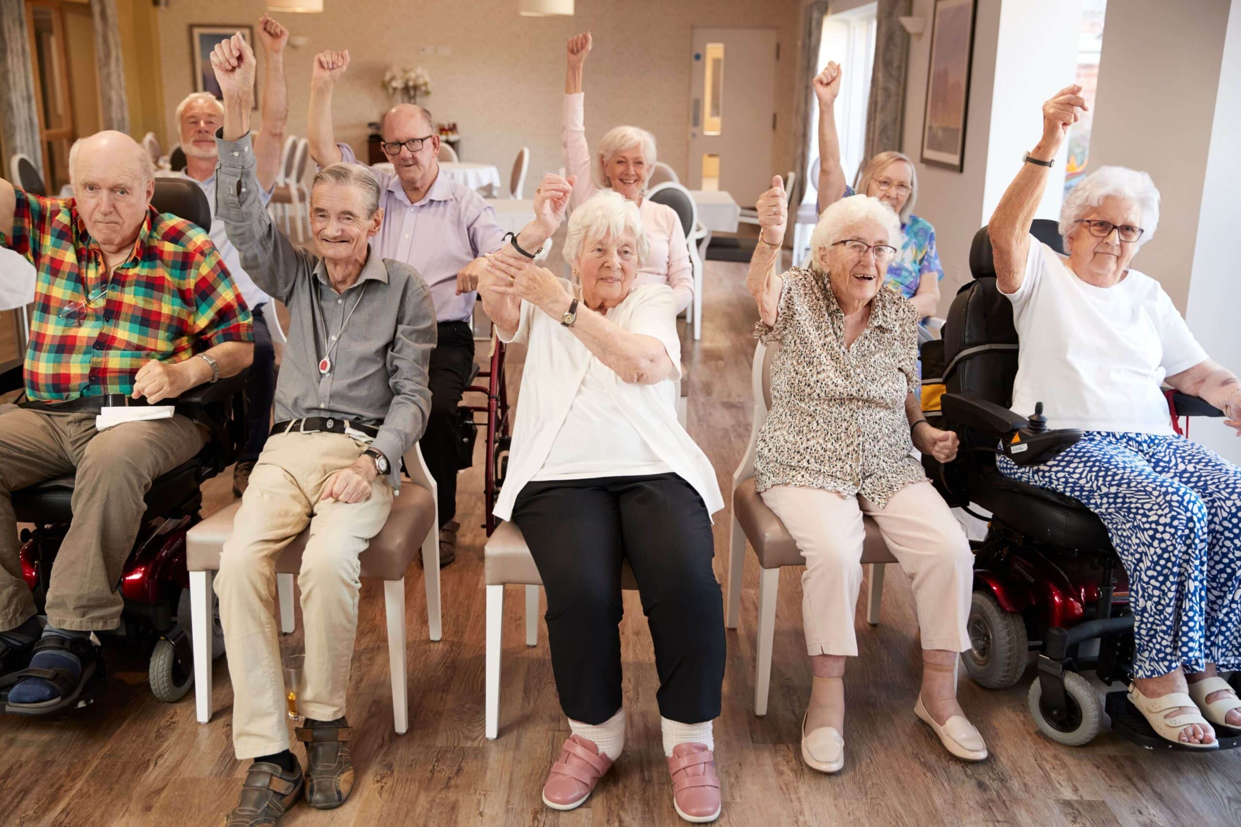 a group of elderly people sitting in chairs with their arms raised