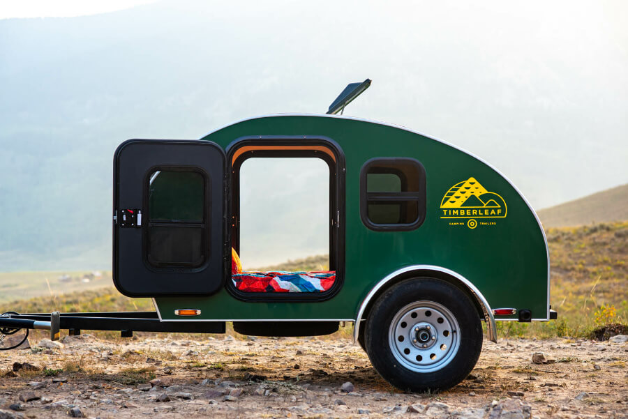 a green trailer with a bed on a rocky surface