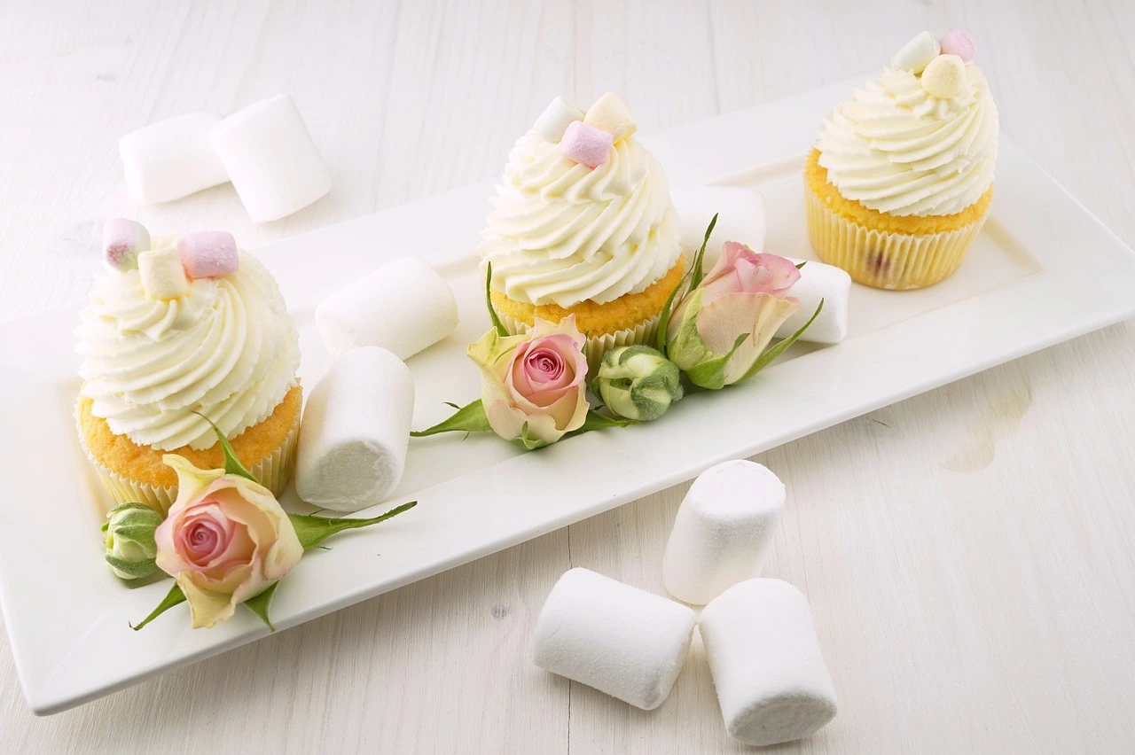 a row of cupcakes with flowers and marshmallows on a white plate