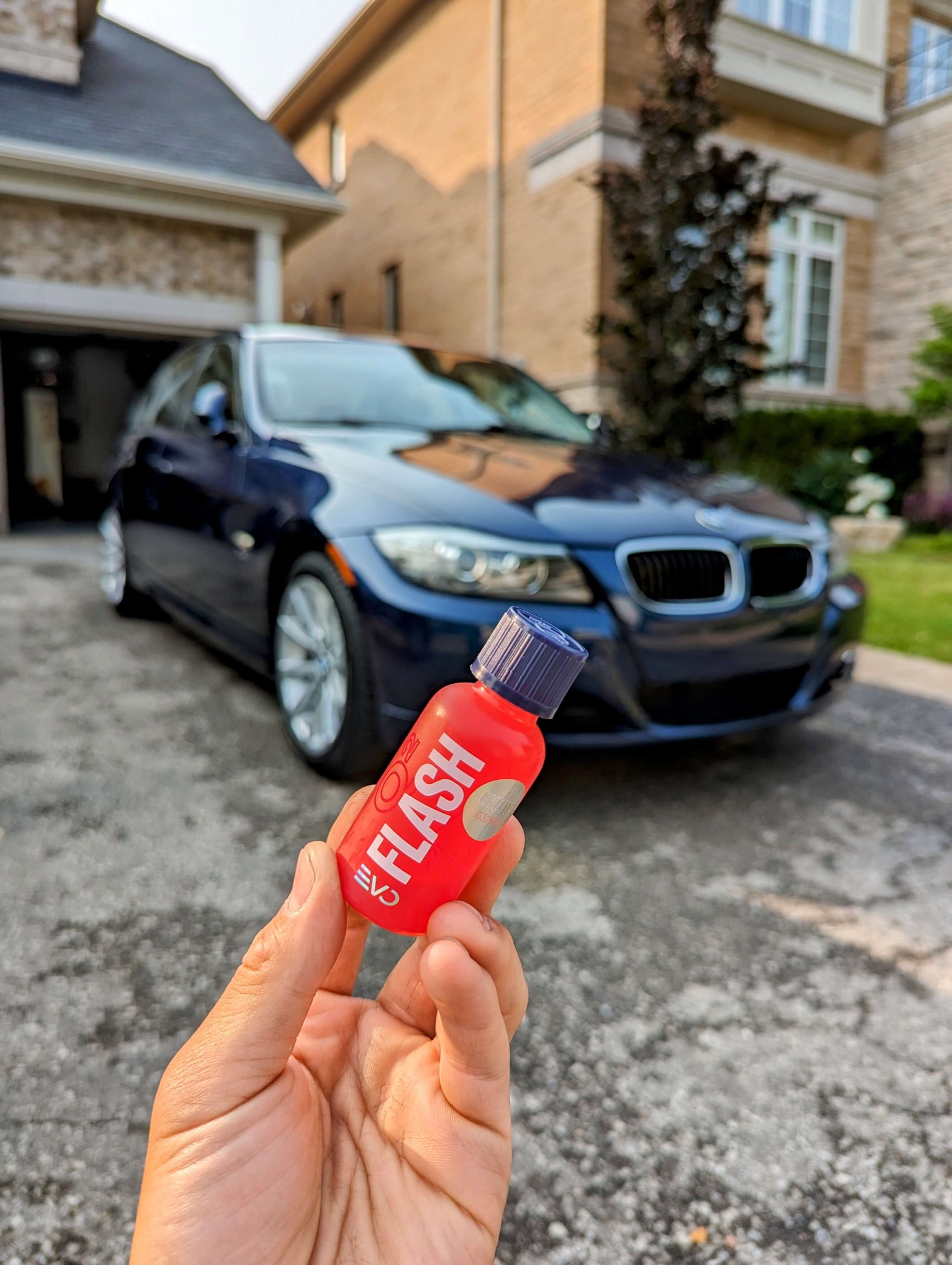 a hand holding a red bottle in front of a blue car