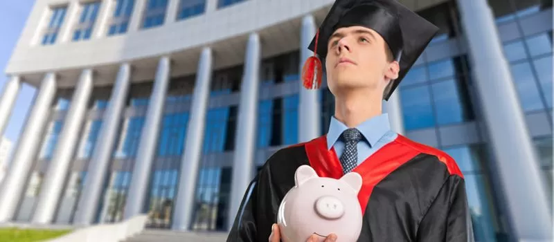 a man in a graduation gown holding a piggy bank