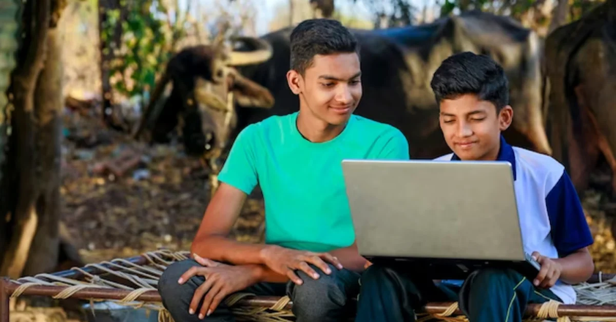 two boys sitting on a wicker chair looking at a laptop