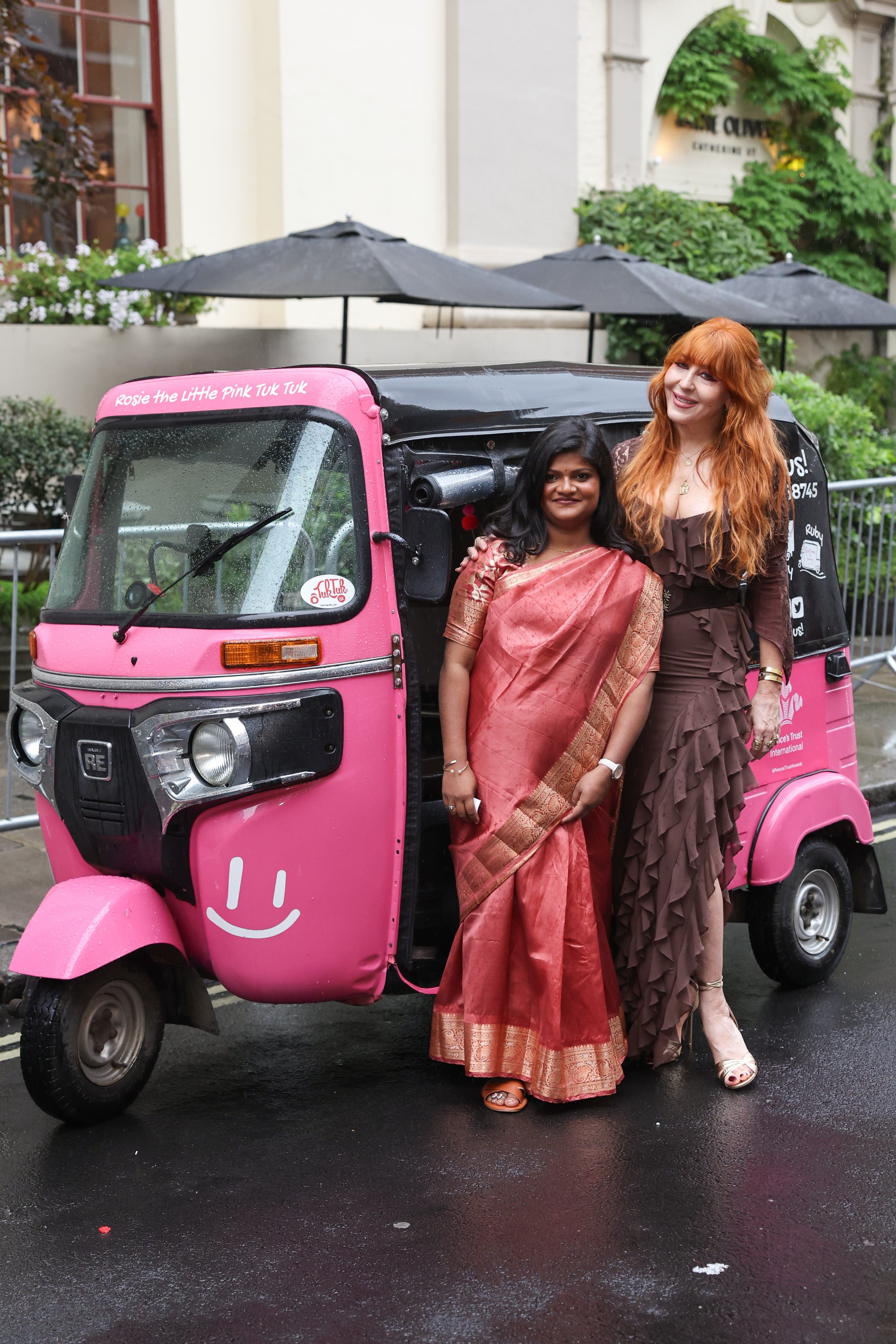 two women standing next to a pink vehicle