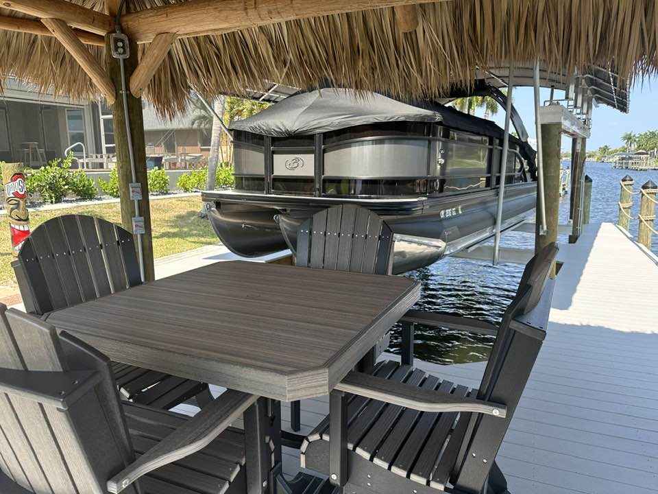 a table and chairs under a shelter with a boat in the water