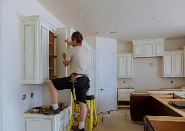 a man on a ladder working on a cabinet