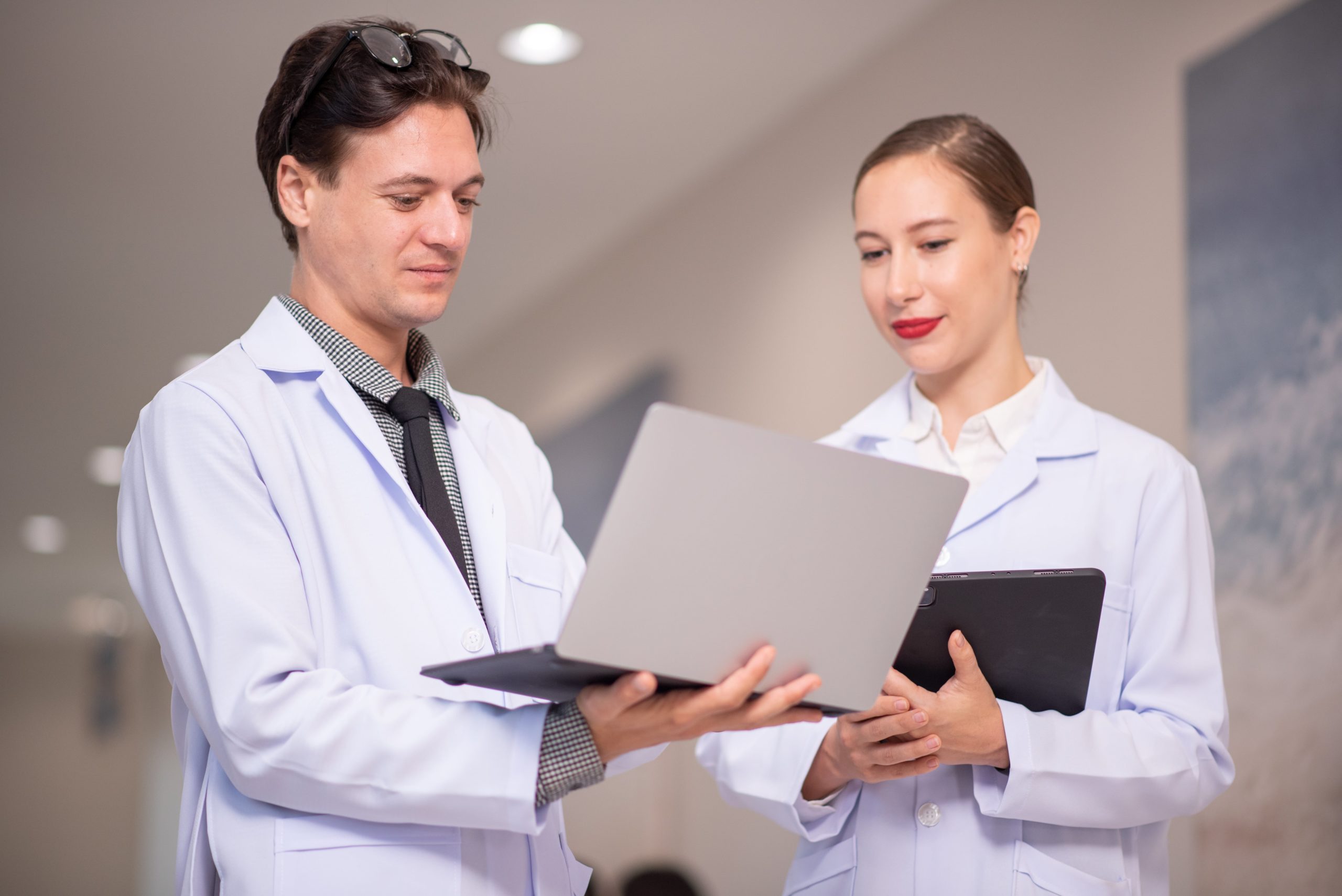 a man and woman in white coats holding laptops