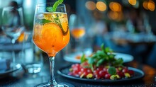 a glass of orange drink with a leafy orange and a green leaf on a plate of food